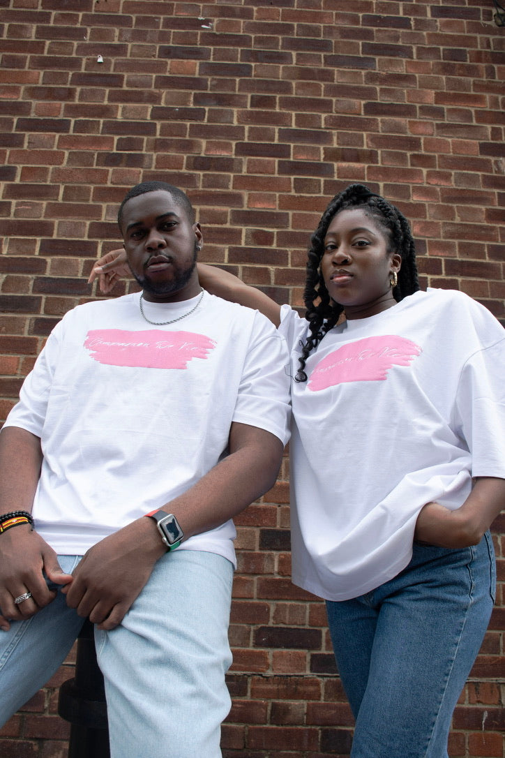 Two people wearing white t-shirts with pink graphics against a brick wall.